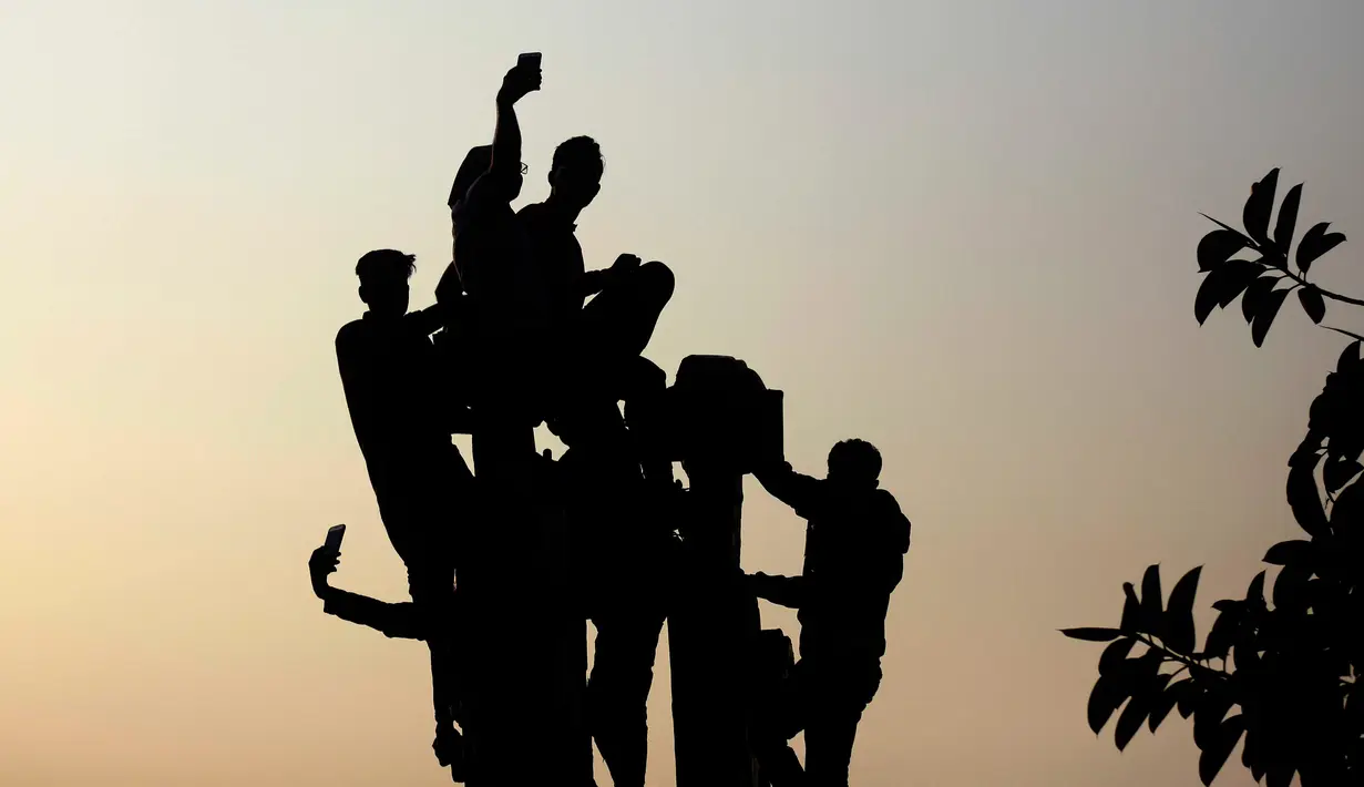 Sejumlah orang menaiki tiang untuk dapat melihat aktor Bollywood, Shah Rukh Khan yang menyapa para fans dari balkon rumahnya di Mumbai, India, Kamis (2/11). Pria yang sering dipanggil SRK ini berulang tahun yang ke 52. (AP Photo/Rafiq Maqbool)