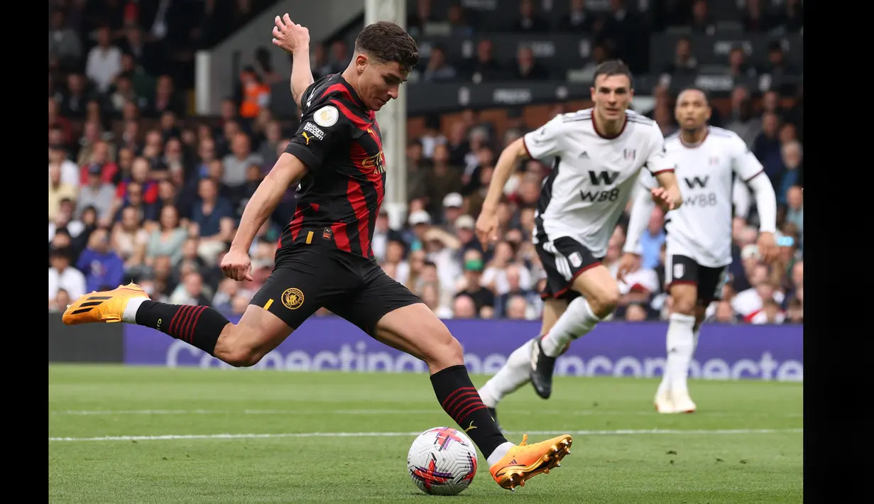 Pemain Manchester City, Julian Alvarez (kiri), menendang bola ke gawang Fulham dalam pertandingan pekan ke-34 Premier League 2022/2023 yang berlangsung di Craven Cottage, Minggu (30/4/2023). Julian Alvarez yang menjadi partner Haaland di lini depan Manc City juga mencetak satu gol dalam pertandingan ini. (AFP/Adrian Dennis)