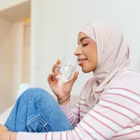 Seorang wanita muslimah mengenakan jilbab pink sedang minum air putih (Foto Dok: Freepik/ stefamerpik).