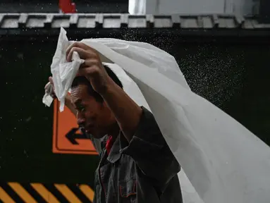 Seorang pria berlindung dari hujan dengan selembar plastik di Beijing, Minggu (30/7/2023). China menempatkan sebagian wilayah utara negara tersebut dalam keadaan siaga merah, termasuk wilayah Beijing, karena hujan lebat yang diperkirakan akan terjadi akibat datangnya topan Doksuri, yang saat ini menghantam bagian lain negara tersebut. (Pedro PARDO / AFP)