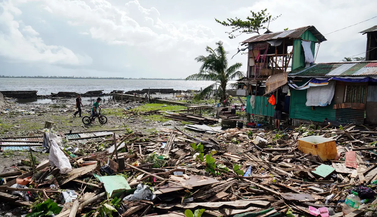 Warga berjalan melewati sebuah rumah yang rusak akibat terjangan topan Phanfone di Tacloban, Provinsi Leyte, Filipina, Rabu (25/12/2019). Topan membuat jutaan warga di negara yang mayoritas beragama Katolik itu merayakan Natal dengan kesedihan. (Bobbie ALOTA/AFP)