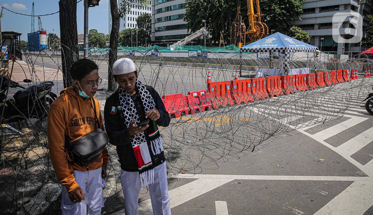 Warga berada dekat kawat berduri di kawasan Jalan MH Thamrin, Jakarta, Kamis (2/12/2021). Polda Metro Jaya memasang barikade di sejumlah titik menuju kawasan Patung Kuda-Monumen Nasional (Monas) Jakarta Pusat guna mengantisipasi kerumunan massa aksi Reuni 212. (Liputan6.com/Faizal Fanani)