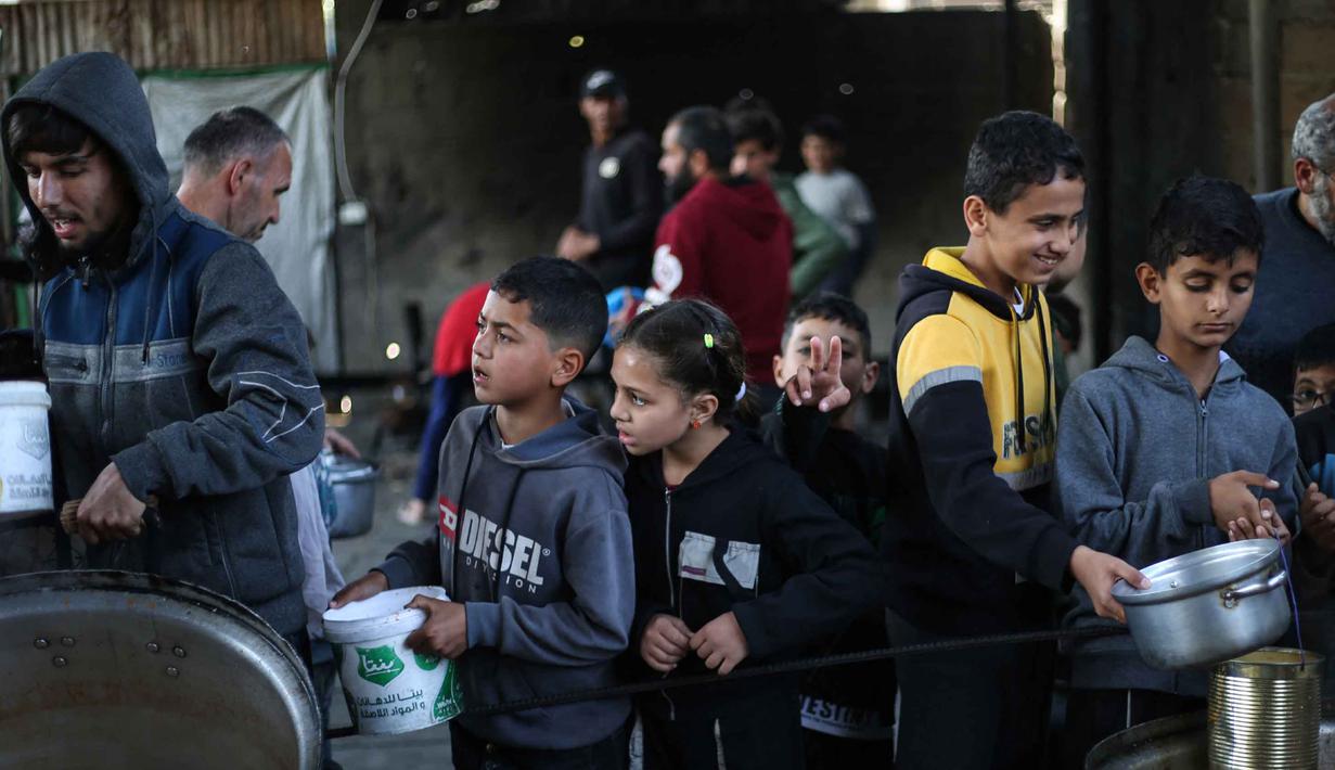 Meski perjanjian gencatan senjata antara Israel dan kelompok Hamas mengizinkan masuknya hingga 600 truk bantuan per hari, otoritas Gaza menyebut volume aktual yang diizinkan hanya sekitar 38 persen dari tingkat pasokan sebelum perang. Tampak dalam foto, anak-anak pengungsi Palestina menunggu untuk menerima makanan dari dapur amal di kamp pengungsi Nuseirat, Jalur Gaza Tengah pada 13 April 2026. (Eyad Baba/AFP)