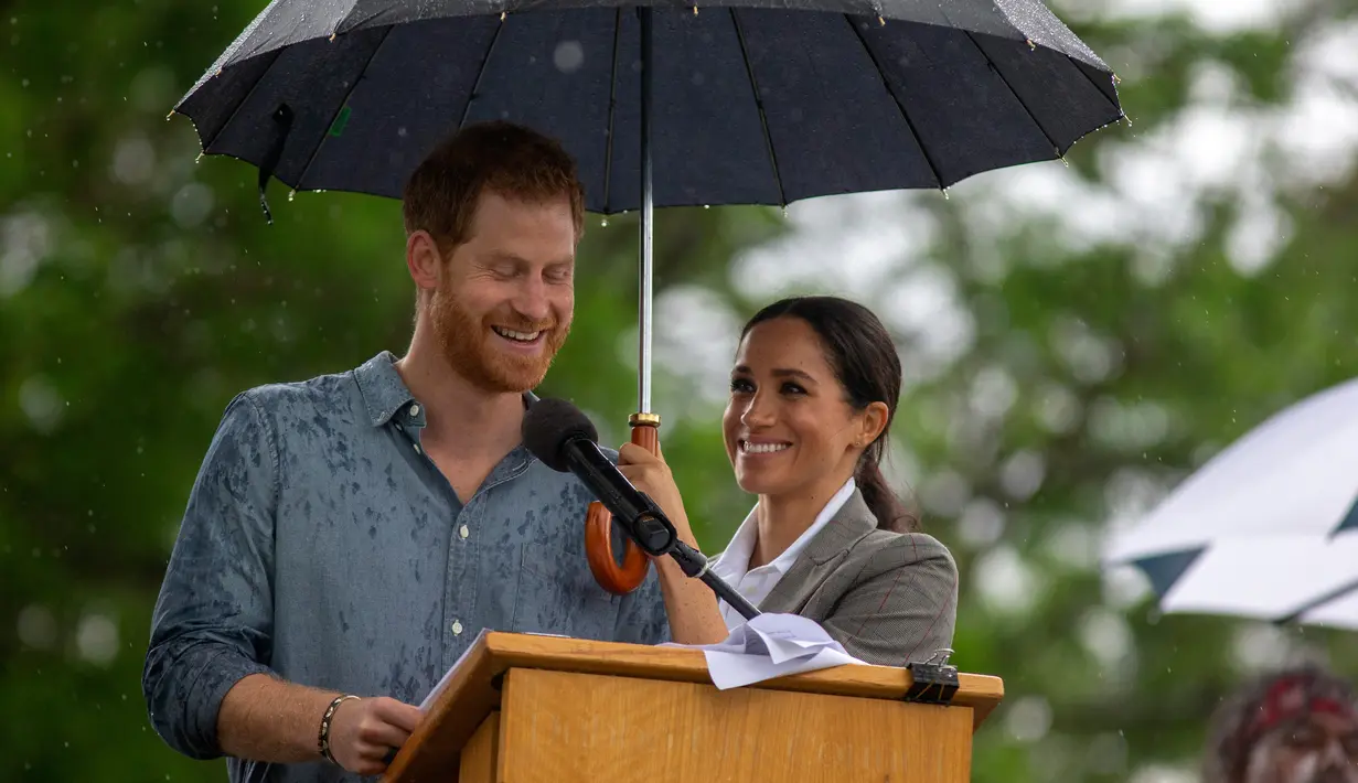 Meghan Markle memayungi Pangeran Harry saat memberi sambutan dalam kunjungan ke Victoria Park, Dubbo, Australia, Rabu (17/10). Keduanya diagendakan tur ke Australia dan Pasifik Selatan selama 16 hari. (Ian Vogler/Pool via AP)