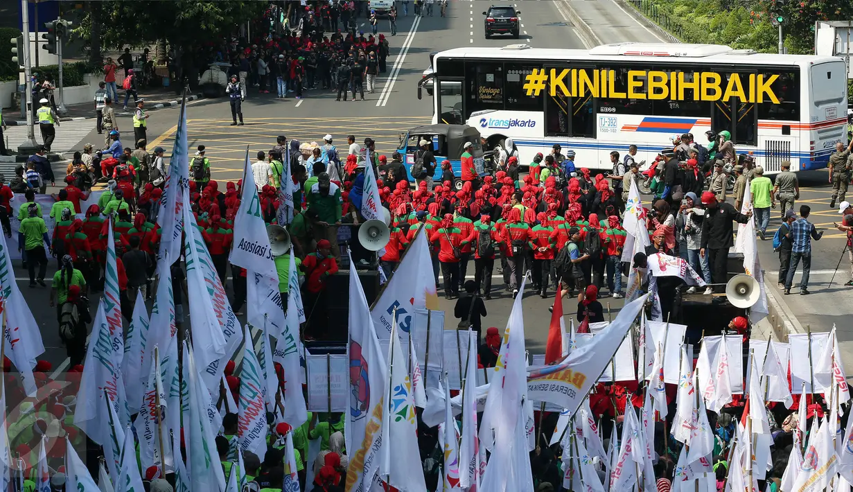 Bus Transjakarta melintas di depan massa buruh yang melakukan aksi peringatan May Day di Jalan MH Thamrin, Jakarta, Senin (1/5). Sambil meneriakkan aspirasinya, massa buruh mulai bergerak menuju Istana Negara. (Liputan6.com/Johan Tallo)