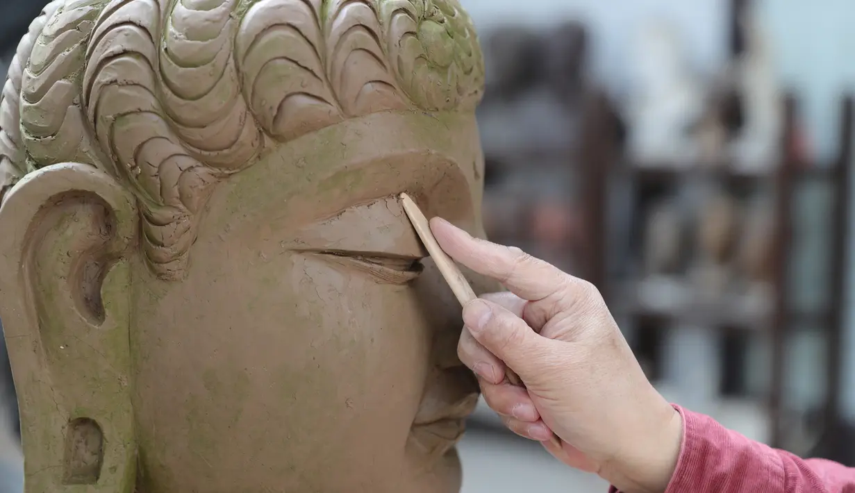 Seniman Du Yongwei menyempurnakan detail sebuah model dari tanah liat sebelum mewarnainya di Dunhuang, Provinsi Gansu, China, Minggu (5/4/2020). Keterampilan seni mewarnai patung masuk dalam daftar warisan budaya tingkat provinsi di Gansu. (Xinhua/Du Zheyu)