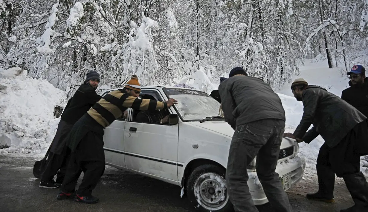 Orang-orang mendorong kendaraan yang terjebak salju di sepanjang jalan Bukit Murree, Pakistan, 9 Januari 2022. Sebanyak 22 wisatawan tewas saat sekitar 1.000 kendaraan terjebak salju tebal di Bukit Murree. (Aamir QURESHI/AFP)