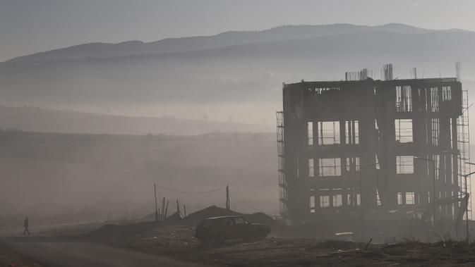 Seorang pria berjalan saat kabut tebal melanda kota Pristina (17/12/2019). Pristina dan banyak kota lain di Kosovo mengalami polusi udara tingkat tinggi. (AFP/Armend Nimani)