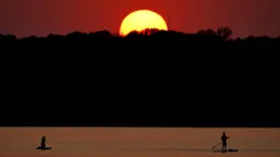 Orang-orang menyaksikan matahari terbenam sambil berperahu di Shawnee Mission Lake, Shawnee, Kansas, Amerika Serikat, Jumat (9/10/2020). Matahari terbenam terus lebih cerah dari biasanya karena asap dari kebakaran hutan barat terus melayang di seluruh negeri. (AP Photo/Charlie Riedel)