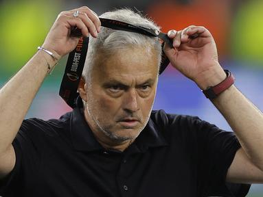 Pelatih AS Roma, Jose Mourinho melepaskan medali dari tubuhnya setelah timnya dikalahkan Sevilla lewat babak adu penalti dalam partai final Liga Europa 2022/2023 yang berlangsung di Stadion Puskas Arena, Hungaria, Jumat (01/06/2023) dini hari WIB. (AFP/Odd Andersen)