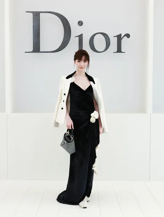 Orm tampil elegan dengan blazer putih dihiasi bros bunga di kerah. Dipadukan dress velvet hitam, tas motif houndstooth hitam-putih, dan heels putih [dok. Dior]