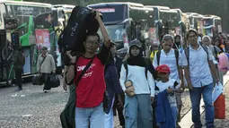 Program bertajuk "Aman Nyaman Bawa Cerita Bahagia" ini menggunakan 709 bus ke 20 kota/kabupaten tujuan. Tampak dalam foto, orang-orang membawa barang-barang mereka saat tiba untuk perjalanan mudik gratis yang diselenggarakan oleh Pemerintah Provinsi Jakarta di Lapangan Monumen Nasional, Selasa 17 Maret 2026. (AP Photo/Achmad Ibrahim)