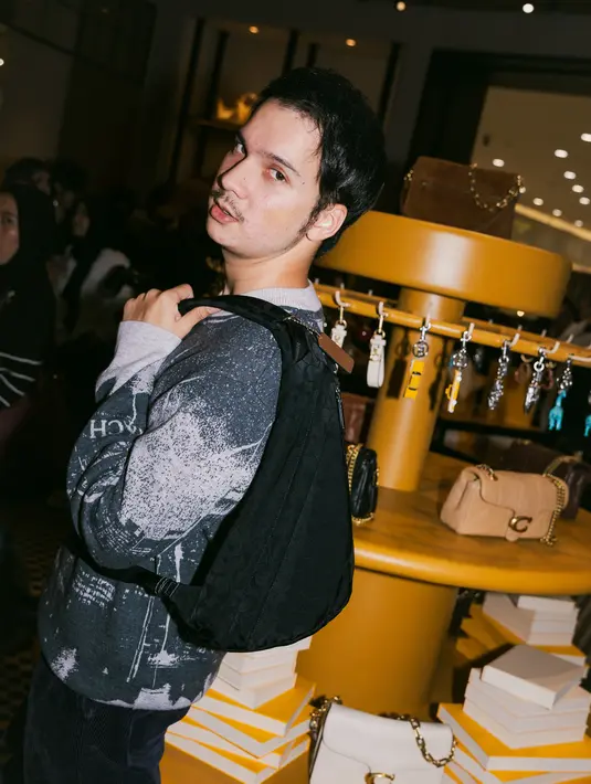 Endy Arfian memilih pendekatan yang lebih playful. Ia mengenakan sweater bermotif dengan backpack hitam sebagai statement piece. Aksen Rexy, maskot ikonik Coach, yang tergantung pada tas memberikan sentuhan fun yang memperkaya keseluruhan gaya. [Dok/KANMO GROUP].