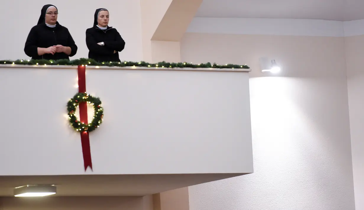 Dua biarawati mengamati dari balkon ketika mereka menghadiri perayaan Misa Natal di sebuah gereja di kota Gjakova, Kosovo Barat (24/12). (AFP Photo/Armend Nimani)