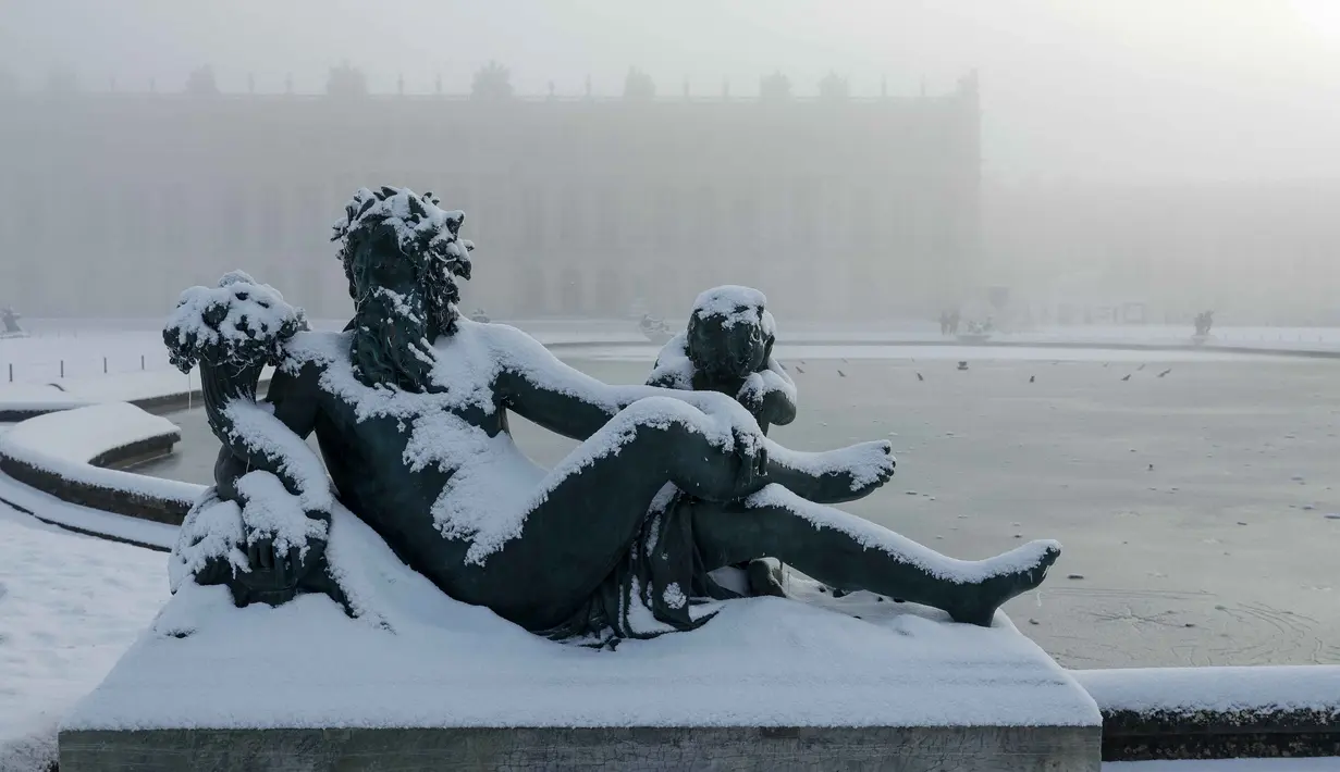 Salju menyelimuti sebuah patung di tepi kolam utara di taman Versailles, luar Kota Paris pada Selasa 6 Januari 2026. Sejumlah negara di Eropa dilanda cuaca ekstrem usai badai salju menerjang wilayah-wilayah tersebut pada Senin, 5 Januari 2026, waktu setempat. (GEOFFROY VAN DER HASSELT/AFP)