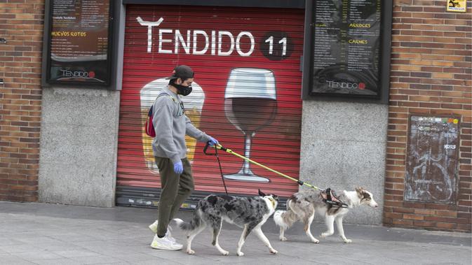 Seorang pria berjalan dengan anjingnya melewati bar yang tutup di Madrid, Spanyol, Selasa (28/4/2020). Pandemi virus corona COVID-19 mengakibatkan tingkat pengangguran Spanyol naik menjadi 14,4 persen pada kuartal pertama 2020. (AP Photo/Paul White)