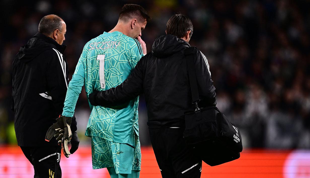 Kiper Juventus, Wojciech Szczesny berjalan meninggalkan lapangan dibantu oleh tim medis setelah mengalami sakit dada ketika pertandingan leg pertama perempat final Liga Europa 2022/2023 melawan Sporting CP di Allianz Stadium, Turin, Jumat (14/04/2023). Szczesny diketahui terkena paltisipasi jantung atau kondisi di mana seseorang merasakan kerja jantung yang kuat, cepat, atau tidak teratur. (AFP/Marco Bertorello)