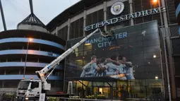 Pekerja memasang poster raksasa bergambar pemain Manchester City terpasang di Stadion Etihad, Manchester, Senin (17/4/2018). Persiapan ini dilakukan untuk merayakan pesta juara Manchester City meraih gelar Premier League. (AFP/Paul Ellis)