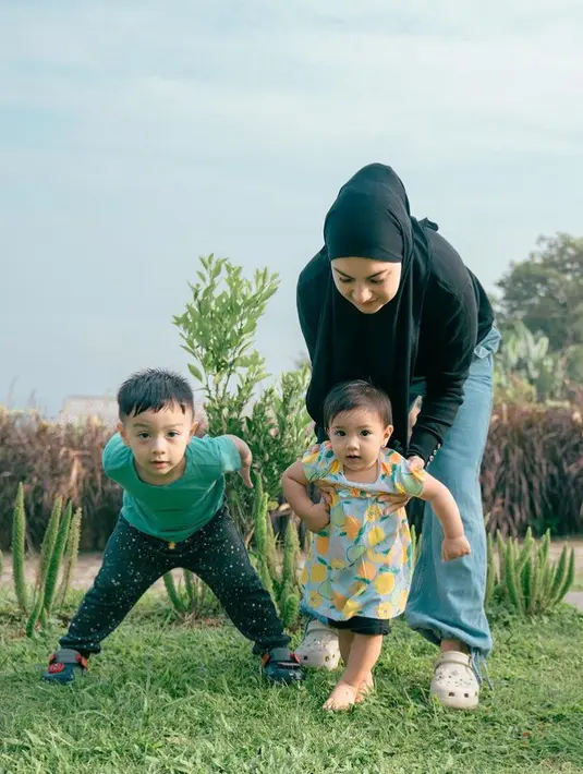 Bermain di outdoor bersama kedua anaknya, Irish tampil santai dengan kerudung dan atasan lengan panjang hitam, dipadukan denim. [ @_irishbella_]