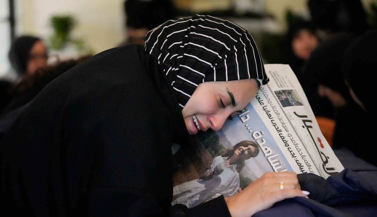 Zainab, saudara perempuan jurnalis Lebanon Amal Khalil yang tewas dalam serangan udara Israel pada Rabu 22 April 2026, memegang koran yang menampilkan potret saudara perempuannya, saat ia berduka di atas peti matinya di desa Baysariyeh, Lebanon Selatan, Kamis 23 April 2026. Jurnalis surat kabar Al-Akhbar, Amal Khalil, ditemukan meninggal dunia imbas serangan udara Israel di Kota al-Tayri, Lebanon Selatan pada Rabu 22 April 2026. (AP Photo/Mohammed Zaatari)