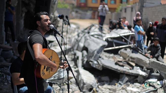 Penampilan seorang penyanyi Palestina selama acara musik di puing-puing bangunan yang baru-baru ini hancur oleh serangan udara Israel di kota Gaza, Selasa (14/5/2019). Aksi itu untuk menyerukan pemboikotan terhadap Kontes Lagu Eurovision 2019 yang diselenggarakan di Israel. (REUTERS/Mohammed Salem)