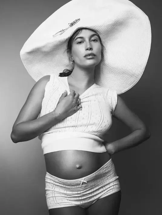 <p>Dalam sebuah foto hitam-putih, terlihat Hailey Bieber dengan baby bumpnya yang semakin membesar mengenakan setelan atasan tanpa lengan dan celana pendeknya, dipadu topi super lebar. [Foto: Instagram/jdblegend_]</p>