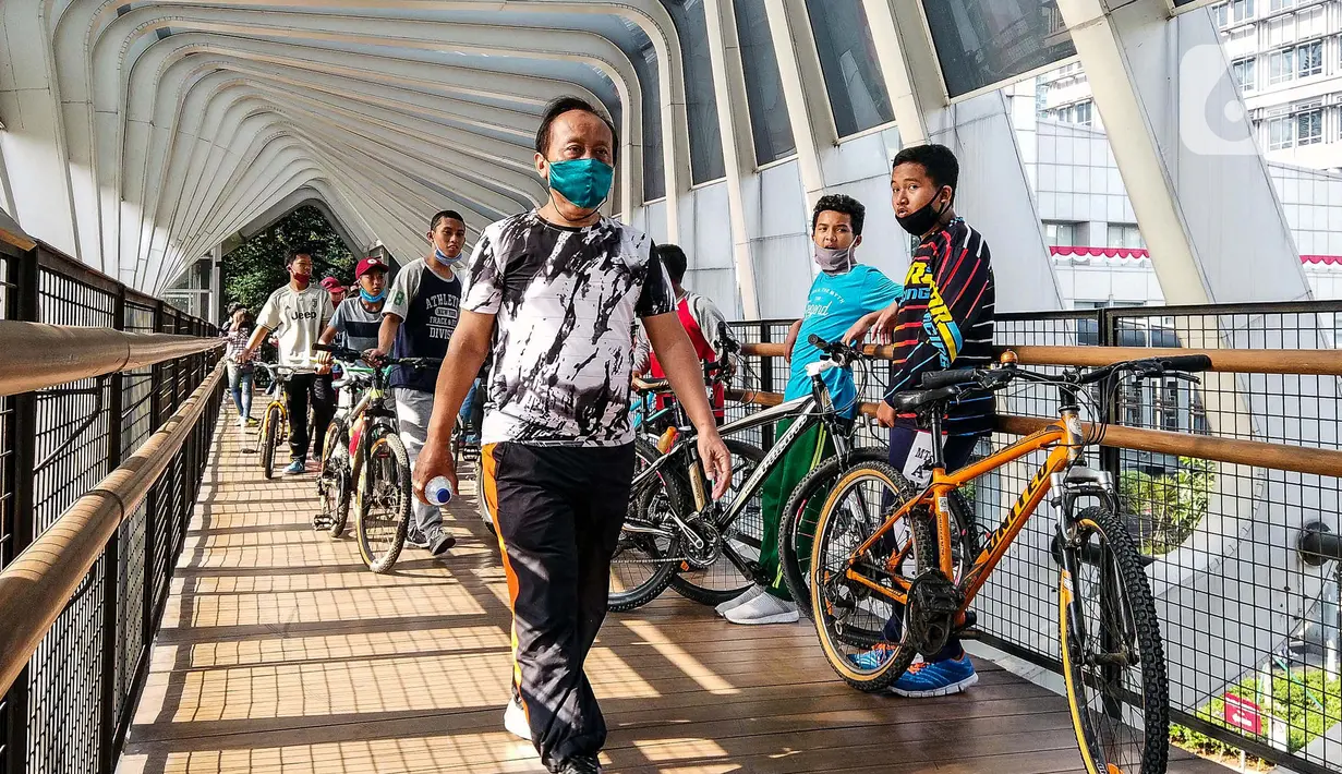 Warga melewati jembatan penyeberangan orang saat berolahraga menggunakan sepeda di sepanjang Jalan Sudirman, Jakarta, Minggu (26/7/2020). Perluasan jalur sepeda sementara dilakukan sebagai dampak peniadaan hari bebas kendaraan bermotor (HBKB) di Jalan Sudirman-Thamrin. (Liputan6.com/Faizal Fanani)