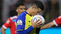 Pemain Al Nassr, Cristiano Ronaldo mencium bola sebelum menendang bola dari titik penalti ke gawang Al Wehda yang membuahkan gol dalam pertandingan lanjutan pekan ke-16 Liga Arab Saudi 2022/2023 yang berlangsung di King Abdulaziz Sports City Stadium, Jumat (10/2/2023) WIB. Kini Ronaldo telah mengemas lima gol dari empat pertandingannya bersama Al Nassr. (AFP)