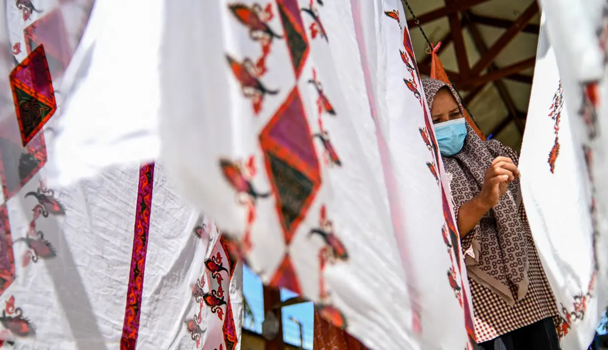 Seorang pekerja mengeringkan kain batik di sebuah bengkel di Banda Aceh, Aceh, Rabu (13/10/2021). Batik Aceh memiliki ciri khas tersendiri, yaitu menggunakan perpaduan unsur alam dan budaya dari masyarakat Aceh sendiri. (Chaideer MAHYUDDIN/AFP)