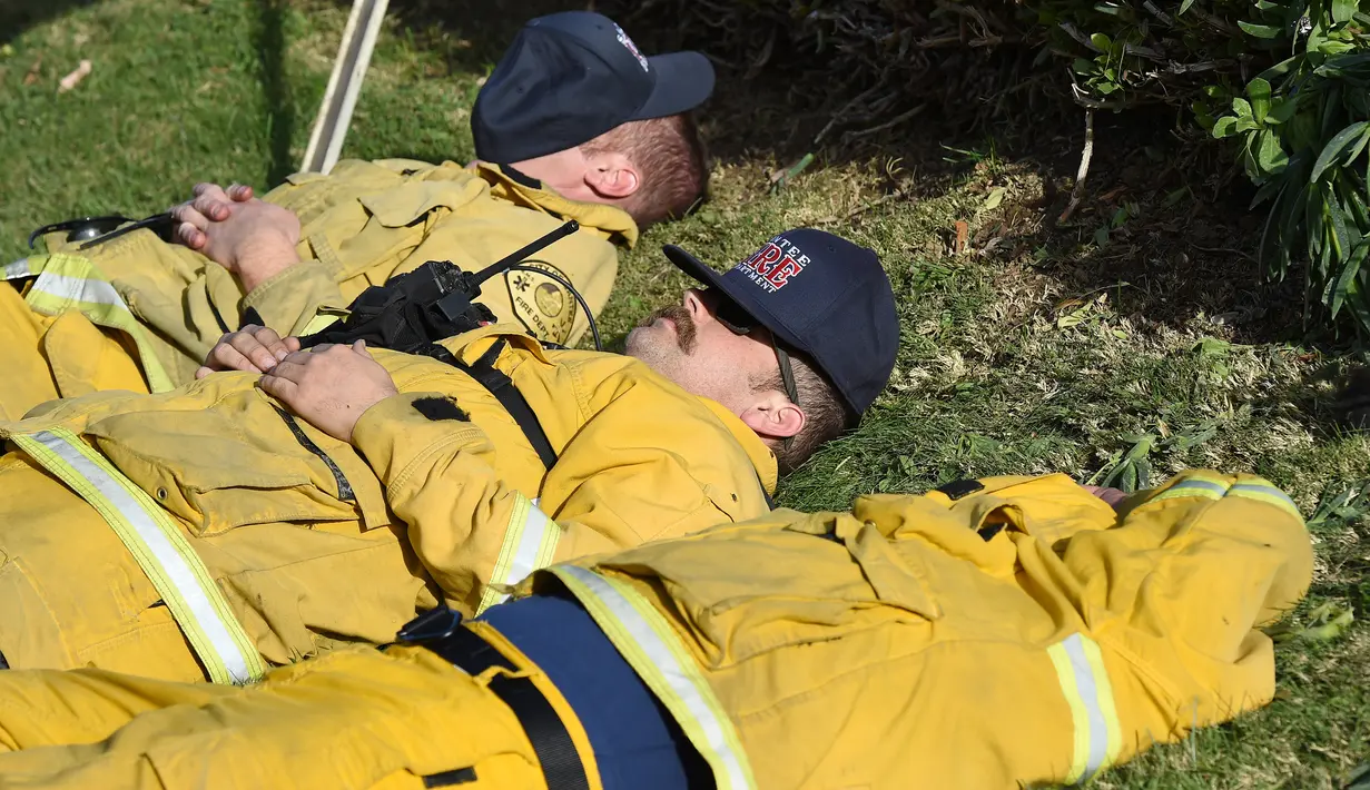 Sejumlah petugas damkar beristirahat setelah berusaha menjinakkan kebakaran yang disebut Lilac Fire di Bonsall, California, Jumat (8/12). Kebakaran yang menghebat karena angin Santa Anna melanda wilayah-wilayah di sepanjang pantai Pasifik (Robyn Beck/AFP)