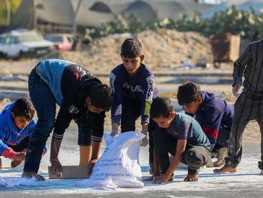 Anak laki-laki Palestina mengais tepung dari jalan setelah sebuah tas jatuh dari truk bantuan yang melaju di jalan Salaheddin di Deir el-Balah di Jalur Gaza tengah pada 5 November 2024. (Eyad BABA/AFP)