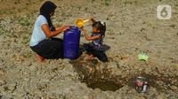 Seorang anak bersama ibunya mengambil air pada galian sumur di tengah aliran Sungai Cihoe, Kamis (28/9/2023). Warga Desa Sukagalih, Jonggol, Bogor, mengalami kesulitan air bersih di tengah fenomena El Nino yang menyebabkan musim kemarau berkepanjangan. (merdeka.com/Arie Basuki)