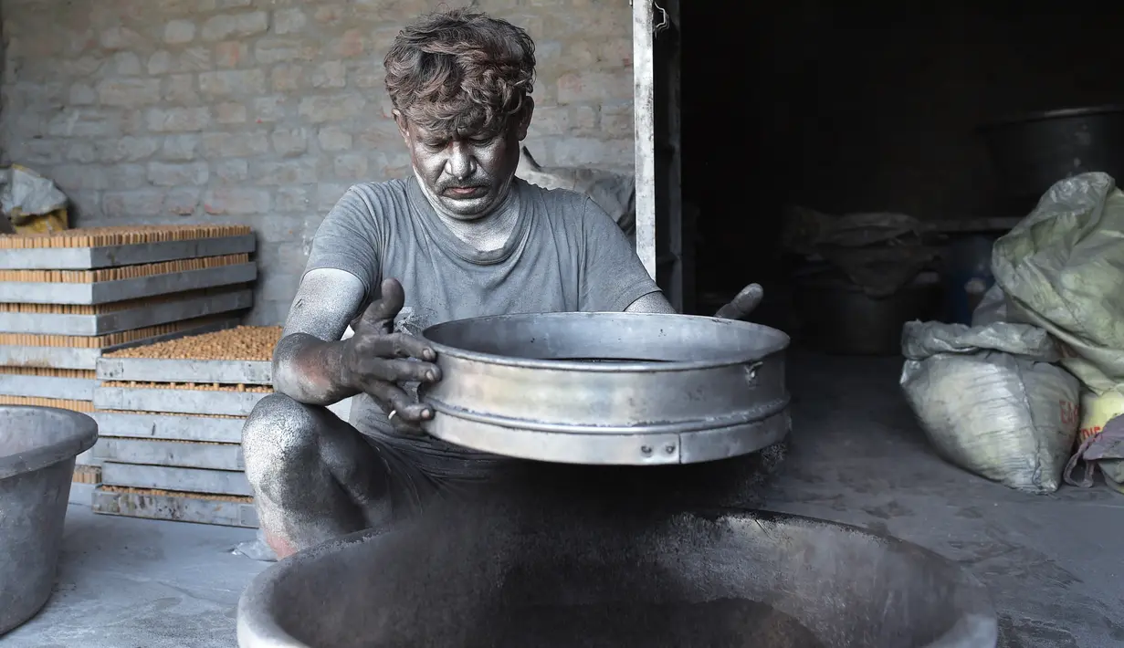Seorang pekerja menyaring bubuk aluminium selama proses pembuatan petasan di sebuah bengkel menjelang festival Diwali di pinggiran Ahmedabad, India (21/9/2022). (AFP/Sam Panthaky)
