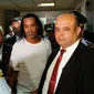 Mantan pemain timnas Brasil, Ronaldinho dikawal oleh polisi meninggalkan kantor pengadilan di Asuncion, ibu kota Paraguay, Jumat (6/3/2020). Ronaldinho bersama saudara laki-lakinya berurusan dengan pihak berwenang Paraguay karena menggunakan paspor palsu untuk memasuki negara itu. (AP/Jorge Saenz)