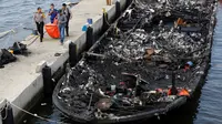 Petugas kepolisian bersama Tim SAR gabungan mengevakuasi kantong jenazah berisi penumpang kapal Zahro Express yang terbakar, di Pelabuhan Muara Angke, Minggu (1/1). Kapal penumpang tersebut terlihat dalam kondisi gosong. (REUTERS/Darren Whiteside)