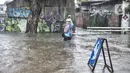 Warga melintasi banjir yang merendam Jalan Abdullah Syafei, Tebet, Jakarta, Kamis (18/2/2021). Hujan deras yang mengguyur sejak pagi tadi menyebabkan aliran Kali Tebet meluap hingga merendam Jalan Abdullah Syafei dengan ketinggian mencapai sepaha orang dewasa. (merdeka.com/Iqbal S Nugroho)