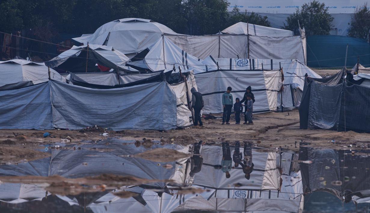 Banjir dengan ketinggian bervariasi merendam permukiman sementara pengungsi Palestina di Gaza. Tampak dalam foto, warga Palestina berdiri di samping area yang tergenang banjir setelah hujan lebat di sebuah kamp pengungsian sementara, Zawaida, Jalur Gaza tengah, Rabu 17 Desember 2025. (AP Photo/Abdel Kareem Hana)