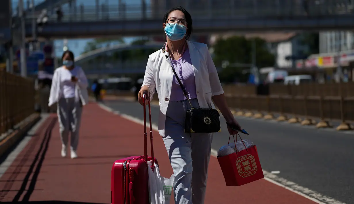 Seorang wanita mengenakan masker berjalan dengan barang bawaannya di jalan saat dia meninggalkan stasiun kereta api Beijing di Beijing, Selasa (6/9/2022). China lockdown jutaan warganya di bawah pembatasan ketat COVID-19 dan melarang warganya lakukan perjalanan domestik pada hari libur nasional yang akan datang. (AP Photo/Andy Wong)