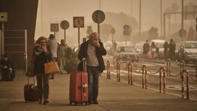 Dua penumpang menutupi hidung dan mulut mereka dari debu badai pasir di bandara Santa Cruz de Tenerife, Spanyol, Minggu, 23 Februari 2020.