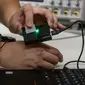 Seorang peneliti mentransfer informasi dari sebuah chip di jam tangan dengan menyentuh sensor yang terhubung ke laptop. Kredit: Purdue University/John Underwood