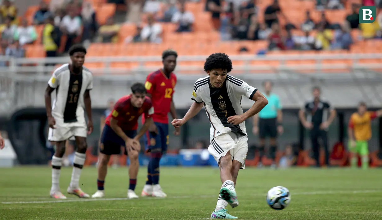 Pemain Timnas Jerman U-17, Paris Brunner (kanan), menendang bola dari titik penalti yang membuahkan gol ke gawang Spanyol U-17 saat pertandingan perempat final Piala Dunia U-17 2023 yang berlangsung di Jakarta International Stadium, Jumat (24/11/2023). (Bola.com/Arief Bagus)