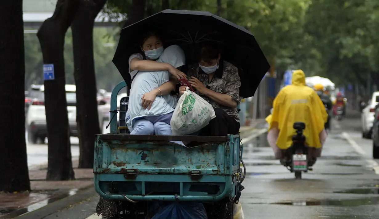 Seorang wanita yang mengenakan masker menggendong seorang anak saat dia mendapat tumpangan saat hujan di Beijing, China, 12 Juli 2022. Beijing telah membatalkan rencana untuk mengizinkan hanya orang yang divaksinasi yang memasuki ruang publik. (AP Photo/Ng Han Guan)