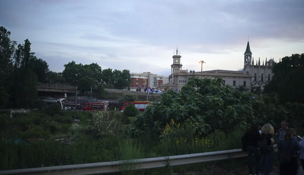 Orang-orang berdiri di jalan di lokasi kecelakaan kereta api di Sant Boi dekat Barcelona, Spanyol, Senin, 16 Mei 2022. Layanan darurat Catalan mengatakan kru membantu mengevakuasi sekitar 100 orang di dalam kereta penumpang. (AP Photo/Joan Mateu Para)