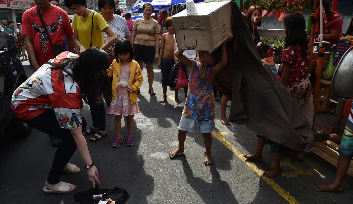 Seorang wanita memberi uang saat anak-anak melakukan tarian singa dengan kepala singa yang terbuat dari kardus saat menghibur pejalan kaki untuk menyambut Tahun Baru Imlek di Manila (4/2). (AFP Photo/Ted Aljibe)