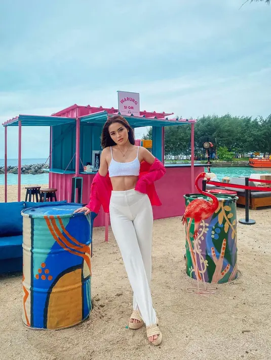 Nicole Parham kali ini berpose di samping tong besar di pantai mengenakan crop top putih dan jaket merah, gaya foto ini membuatnya terlihat seksi. (Instagram/ nicoleparham_)
