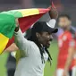 Pelatih Senegal, Aliou Cisse melakukan selebrasi sambil membentangkan bendera Senegal usai memastikan menang adu penalti 4-2 (0-0) atas Mesir dalam laga final Piala Afrika 2021 di Stade d'Olembe, Yaounde, Kamerun (6/2/2022). (AFP/Kenzo Tribouillard)