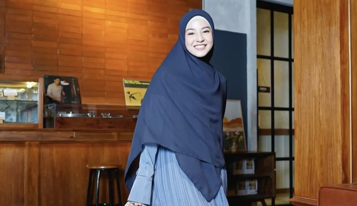 Tampil serba biru dengan kerudung yang cocok dipadukan dress plisket warna biru denim sambil membawa sling bag. [@natasharizkynew]