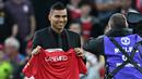Casemiro yang berpakaian serba hitam, mulai dari jas sampai kemeja yang dikenakannya, berjalan menuju tengah lapangan. Di sana, ia memamerkan jersey barunya yang masih belum ada nomor punggungnya itu. (AFP/Paul Ellis)