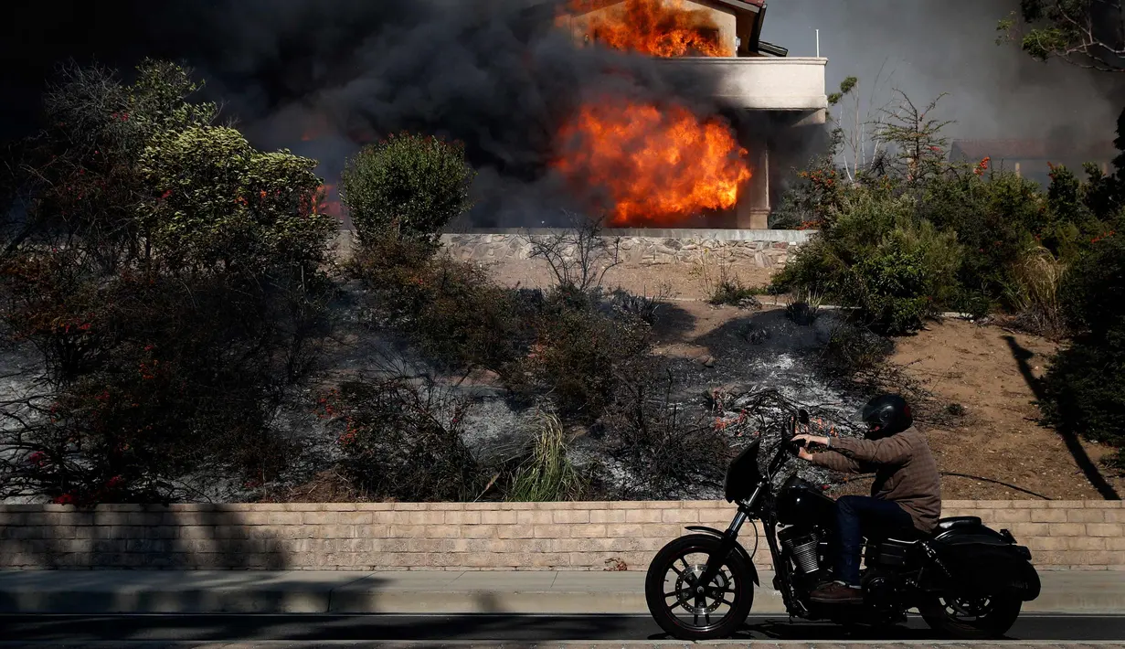 Seorang pria mengendarai motor melewati sebuah rumah yang terkena dampak kebakaran di Ventura, California, AS (5/12). Dipicu oleh angin kencang Santa Ana, api merambat dengan cepat dan merusak sekitar 26.000 hektare. (AP Photo / Noah Berger)