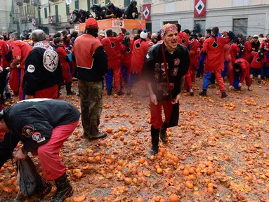 Peserta berjalan di atas tumpukan jeruk yang hancur pada festival "Battaglia delle Arance" (Perang Jeruk) di sebuah kota kecil di Provinsi Turin, Italia, Minggu (11/2). Tradisi melempar jeruk dilakukan selama tiga hari pada Februari. (MIGUEL MEDINA/AFP)
